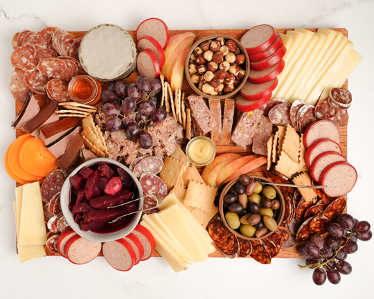 Assorted charcuterie board with meats, cheeses, fruits, and nuts on a wooden board.