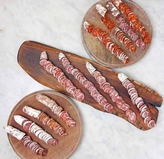 A variety of sliced salamis arranged on wooden boards, showcasing different colors and seasoning.