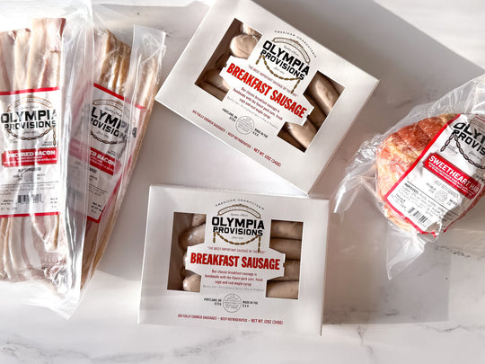 two packs of olympia provisions breakfast sausage and uncured bacon and an olympia provisions sweetheart ham