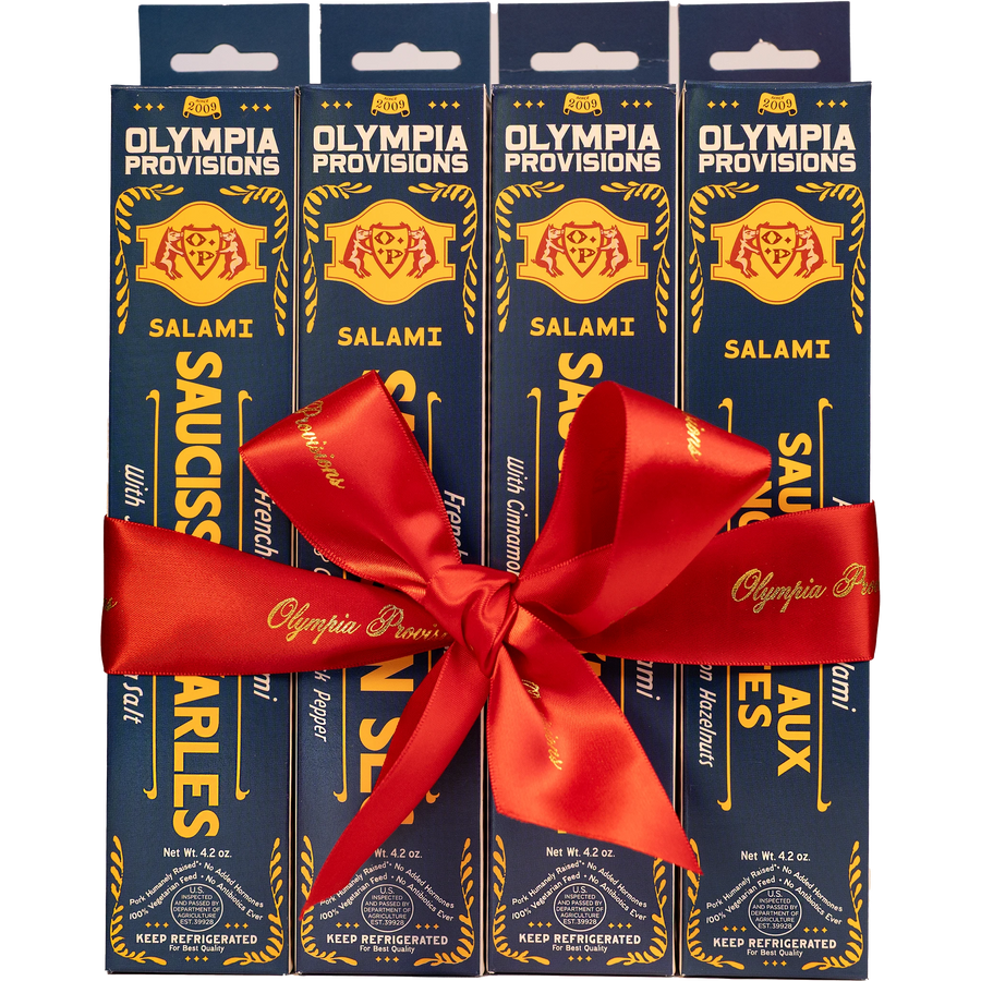 Four blue boxes of Olympia Provisions French-inspired Salami, wrapped in a large red ribbon bow.