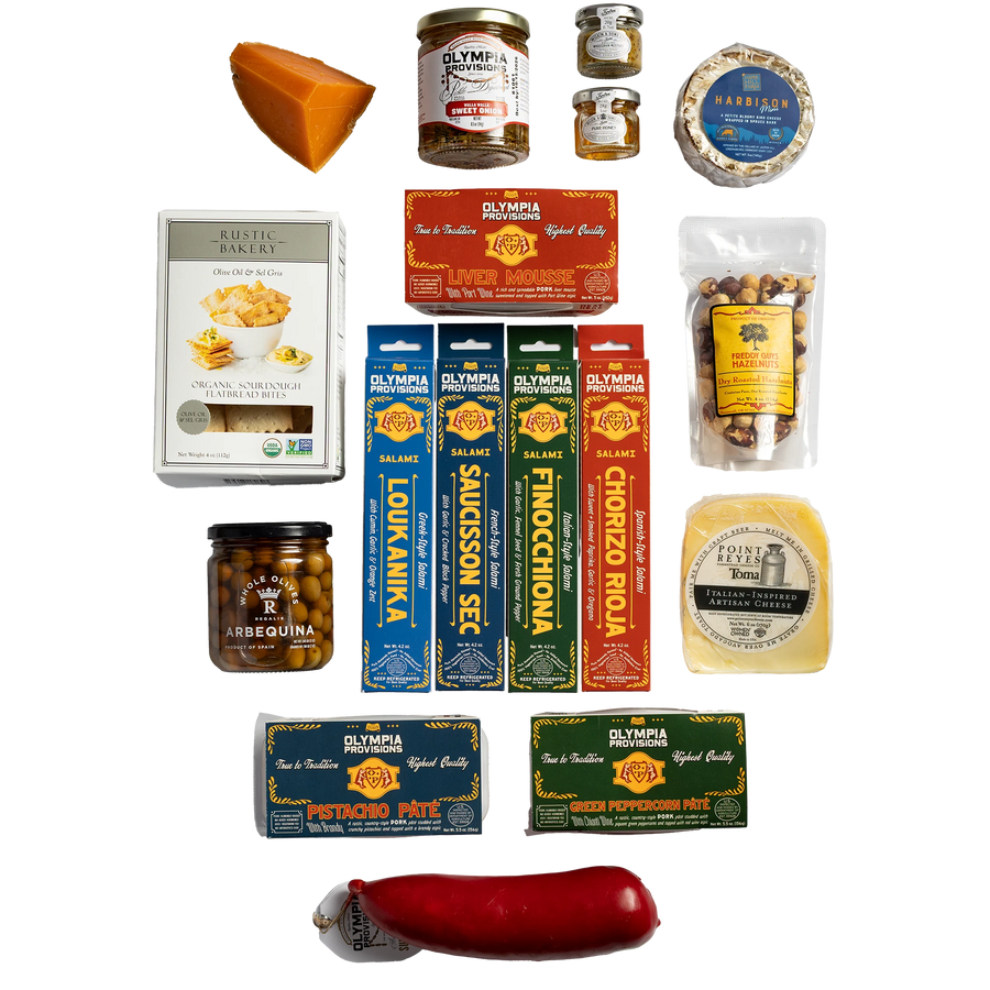 A curated assortment of gourmet food products including: four European-inspired Olympia Provisions salamis, two country-style pates, one red summer sausage, a jar of sweet onion pickles, a jar of olives, three cheeses, crackers, hazelnuts, and two small jars of preserves.