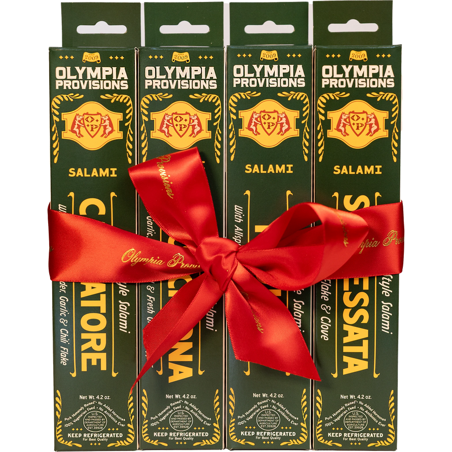 Four green boxes of Olympia Provisions Italian-inspired Salami, wrapped in a large red ribbon bow.