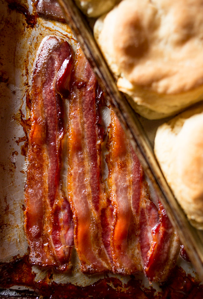 a tray of bacon slices underneath a tray of biscuits