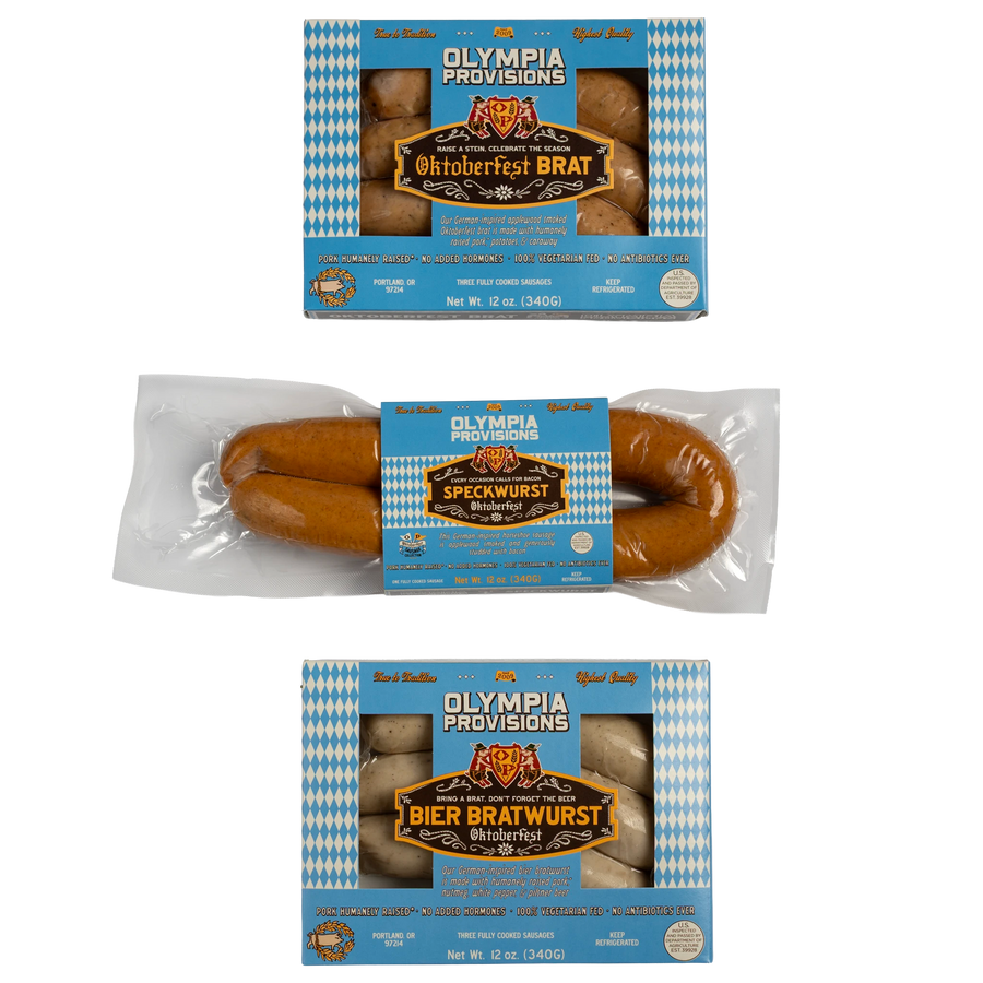 Three packages of Olympia Provisions bratwurst sausages shown on a transparent background: Oktoberfest Brat, Speckwurst, and Bier Bratwurst all with blue and white packaging.