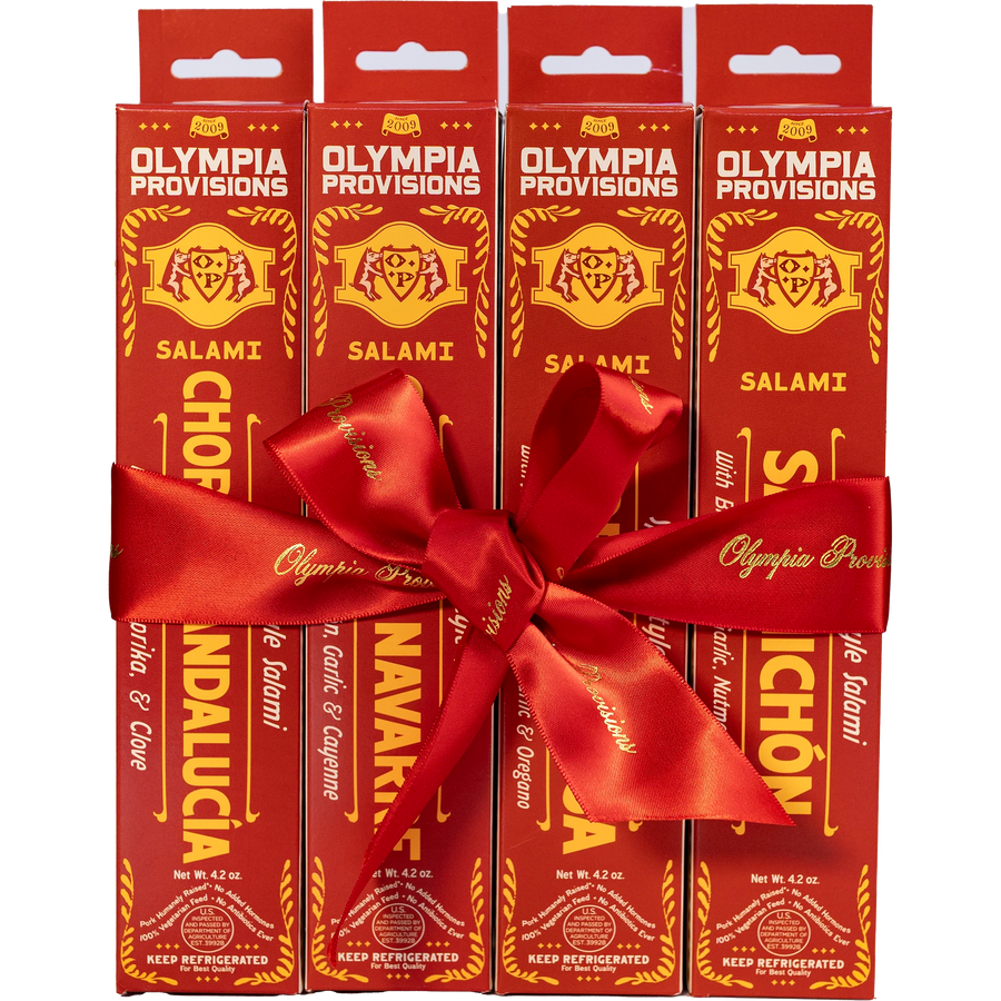 Four red boxes of Olympia Provisions Spanish-inspired Salami, wrapped in a large red ribbon bow.