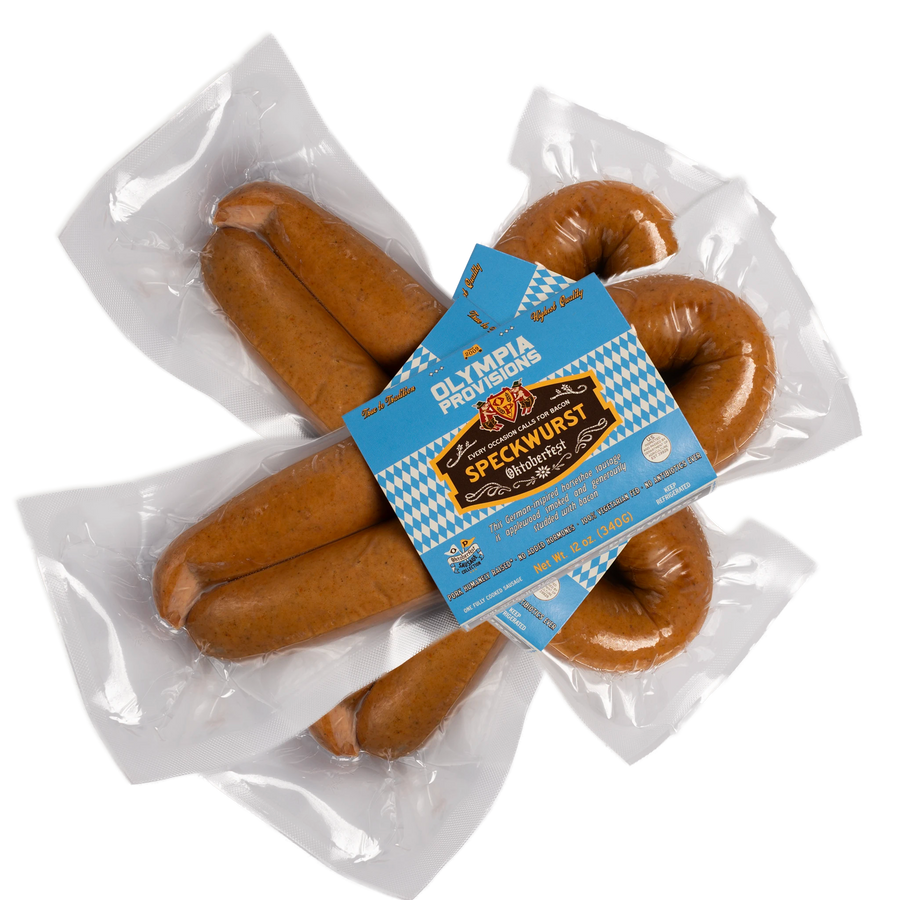 Three packs of Olympia Provisions Speckwurst sausages stacked on a transparent background. The packaging features a blue and white diamond pattern.