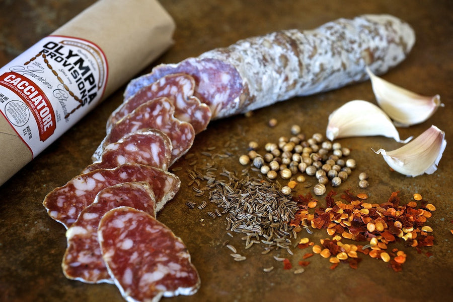 Olympia Provisions Cacciatore sausage sliced next to an arrangement of spices